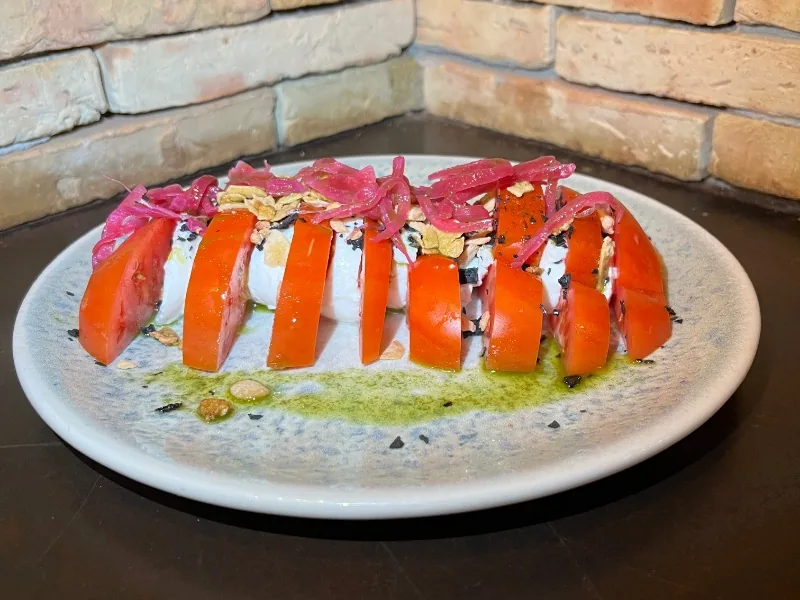 Mozarella and fresh tomato salad with basil oil, almond crunchy and pickled onion