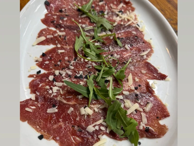 Aged beef carpaccio seasoned with EVOO, truffle oil, parmesan, and arugula